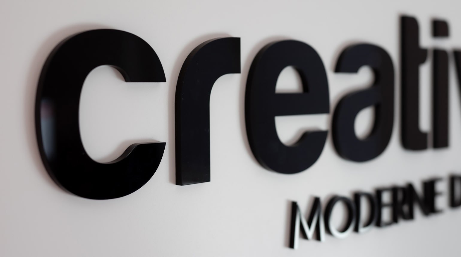 Schwarze, plastische Buchstaben an weißer Wand formen "creativ", darunter teils "MODERNE" sichtbar.