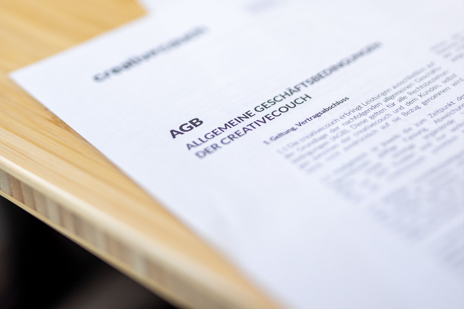 Nahaufnahme eines Dokuments mit Titel "AGB Creative Couch" und DSGVO-Hinweis auf hellem Holztisch.