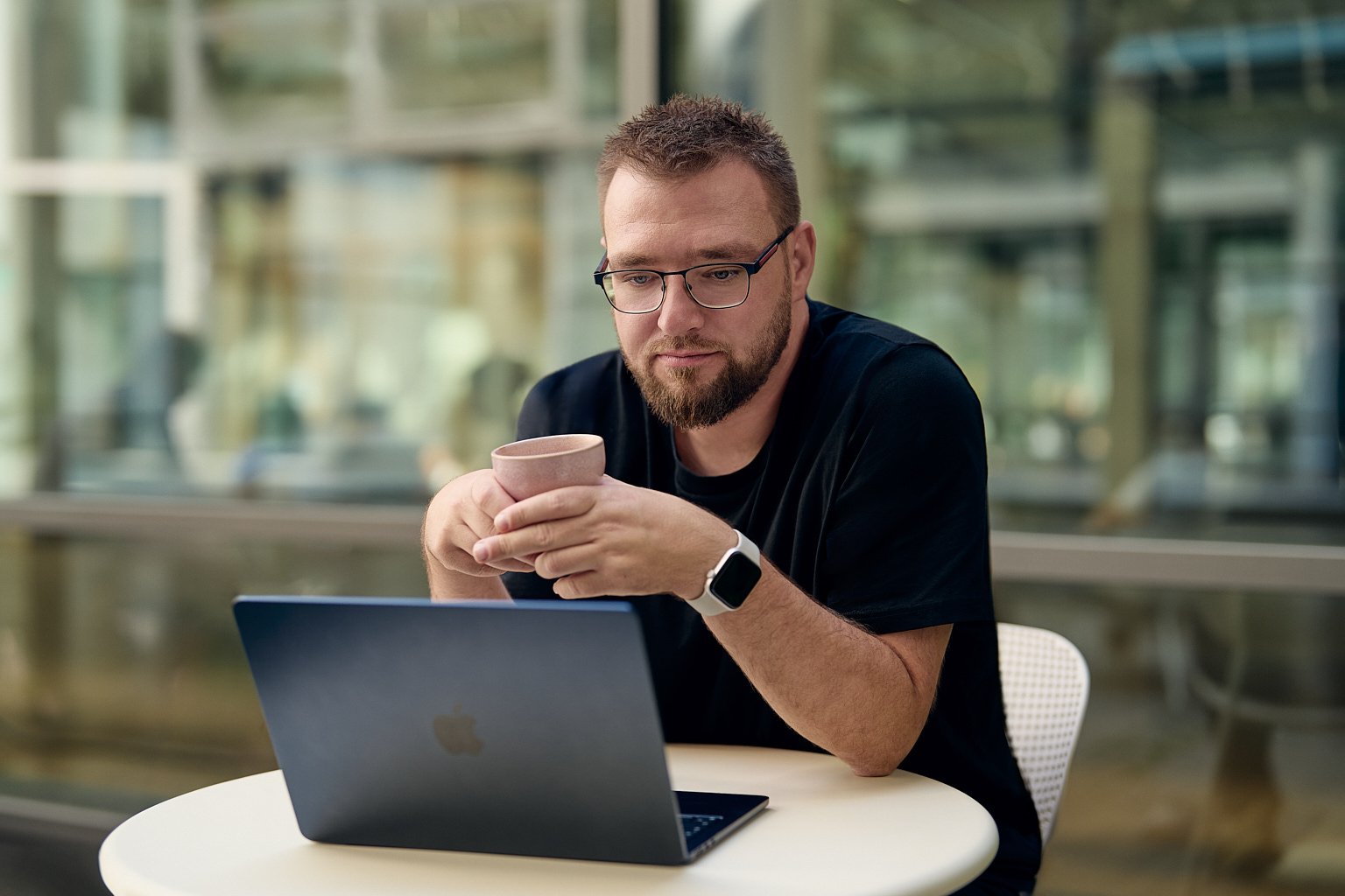 Ein Mann mit Brille sitzt am Tisch, hält eine Tasse und schaut auf einen Laptop vor sich. Ein Mann mit Brille sitzt am Tisch, hält eine Tasse und schaut auf einen Laptop vor sich.